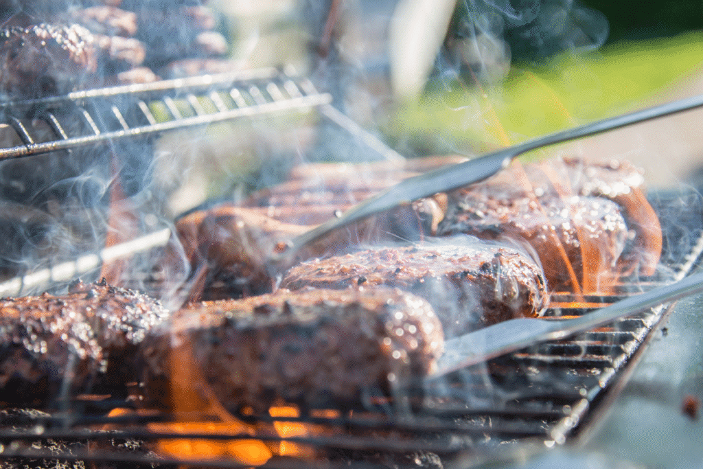 Grillen von Fleisch – Rauch und hohe Temperaturen Mehrere Fleischstücke auf einem Grillrost mit Flammen und Rauch