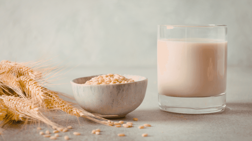Ist Hafermilch gesund? Hafermilch in einem Glas neben Haferkörnern und Getreide auf einem Tisch