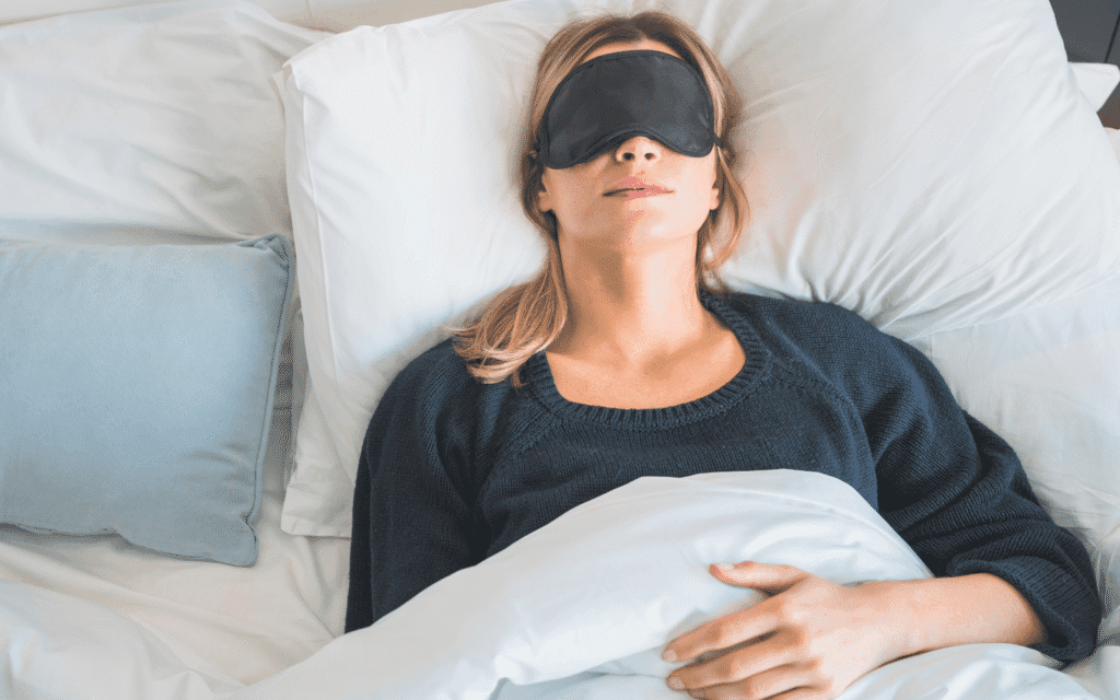 Schlafphasen verstehen: Frau mit Schlafmaske im abgedunkelten Schlafzimmer für besseren Schlaf
