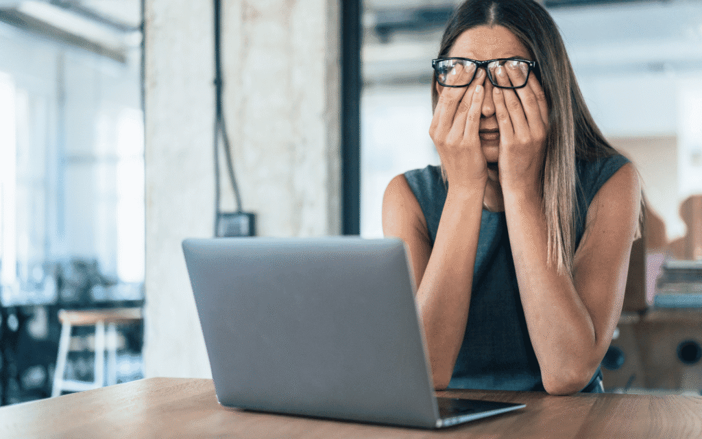 Ständig müde: Müde Frau mit Brille reibt sich am Laptop die Augen, erschöpft nach langer Bildschirmarbeit.