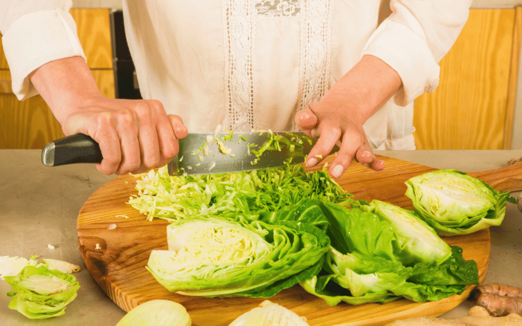 Sauerkraut selber machen: Hände schneiden frischen Weißkohl mit einem Messer auf einem Holzbrett.